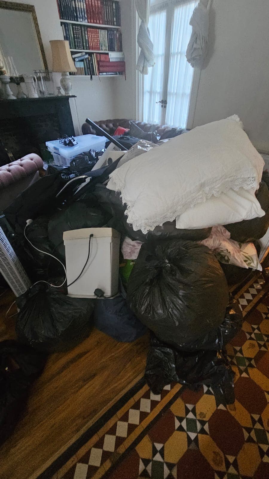 Cluttered living room with a large pile of black trash bags topped with white pillows.